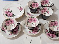 Full set with 6 cups arranged on matching saucers and stacked cake plates showing floral design and black cup exteriors.