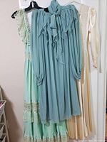 Three vintage dresses displayed hanging on a door, showing different colors and styles: off-white satin dress, mint green lace and pleated dress, and light blue ruffled dress.