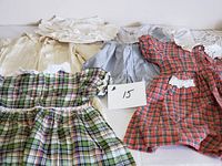 Four toddler dresses arranged flat, showing a variety of patterns and styles including plaid and solid colors with lace accents.