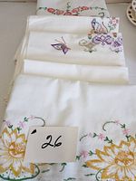 Vintage pillowcases laid out stacked, showing embroidered floral and butterfly designs along with crochet edges.