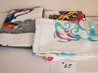 Three vintage printed tablecloths folded and laid out, showing edges with measurement tags.
