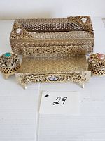 Full view of three vintage vanity accessories: napkin/tissue holder and two footed trinket boxes all in gold tone filigree with jeweled accents