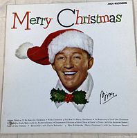 Front cover of Bing Crosby Merry Christmas vinyl record, shows Bing Crosby in Santa hat and colorful 'Merry Christmas' text.
