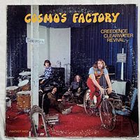 Front cover photo of Creedence Clearwater Revival's "Cosmo's Factory" vinyl album showing band members with bicycle and musical instruments in a room with red carpet.
