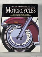 Front cover of The Encyclopedia of Motorcycles showing a detailed motorcycle wheel and fork illustration with text about the book's contents and editor Roger Hicks.