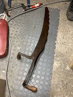 Full view of the antique hay saw showing the rusted metal blade with large teeth and wooden handles