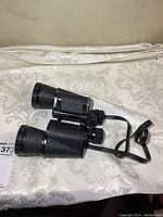 Side view of black textured vintage binoculars showing overall design and strap attached.