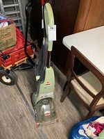 Full view of green Bissell Quick Steamer carpet cleaner standing upright with power cord wrapped on the handle, placed on wood floor