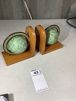 Pair of wooden bookends, each with a green turning globe, light wood finish, approx 6 inches tall from a side angle.