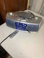 Front angled view of silver JVC boombox with cassette deck, CD player, and remote on white surface, radio working confirmed.