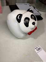 Side angle view of porcelain panda cookie jar showing black ears, eyes and red bow tie.