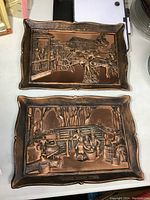 Full view of the pair of framed copper art plaques showing raised relief scenes.