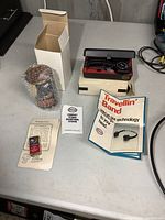 Overview photo showing both Esso Uniflo can radio in bubble wrap with box, Esso headphone radio set in case, and related paper manuals and brochures on gray table.