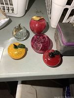Set of 4 hand blown glass fruit paperweights arranged on a table, varying sizes and colors including clear, red, and yellow-orange