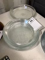 Seven clear glass pie plates stacked and displayed to show quantity and condition.