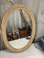 Full front view of the oval mirror showing the carved floral and scroll detailed frame and reflective surface.