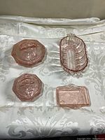Top view of four pink glass dishes: two small lidded candy dishes, one oval handled dish, and a rectangular ashtray.
