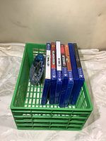 Eight PS4 video games and one loose disc in a green basket, showing game cases and one disc without case