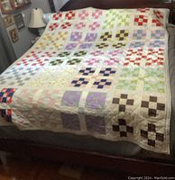 Full view of quilt spread on bed showing multi-colored patchwork blocks on cream background