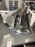 Front and side views of a polished aluminum sailboat sculpture highlighting its smooth reflective surface and modern design.