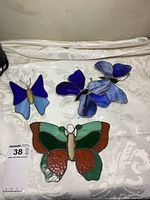 Four stained glass butterflies of different sizes and colors on a white fabric surface.