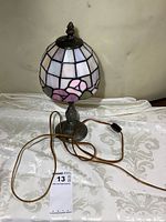 Full view of stained glass table lamp showing shade and metal base with cord and inline switch.