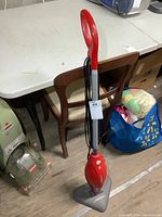 Full side view of red Dirt Devil steam mop standing upright on floor, shows handle, base, and cord wrapped around handle.