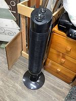 Tall black tower fan upright on floor showing front grille and base
