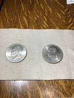 Two 1976 US Bicentennial silver dollar coins laid on white cloth on wooden surface showing obverse side with profile of President Eisenhower.
