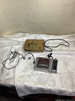 View of JVC cassette player with radio tuner, carrying case, and ear buds on white fabric.