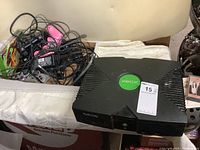 Original Xbox console on table with controllers and cables beside it, showing top view with Xbox logo.