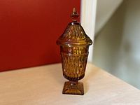 Amber Indiana Glass Mount Vernon apothecary candy dish with lid shown against red background on table.