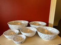 Six blue confetti patterned mixing bowls arranged in a cluster against a red background, showing graduating sizes.