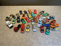 Top view of all 34 toy cars arranged on a table, displaying a wide variety of colors and models including sports cars, trucks, and motorcycles.