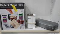 Photo of the Perfect Blend Pro box, the white Cuisinart coffee grinder with silver lid held by a rubber band, and the long metallic Hamilton Beach sharpener.
