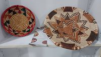 Two handcrafted African coiled baskets displayed on a white shelf, showing patterns and colors