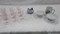 Full lot showing the pink etched Depression glass stemware, the ceramic hen dish, two pastel-striped bowls, and one Asian duck ceramic mug.