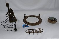 All four items: the bronze lamp, brass porthole mirror, brass sailboat key hook, and brass lighthouse trinket dish with lid, arranged together on white background.
