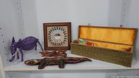 Shelf display showing all five cultural and decorative items including the purple wire elephant, framed Navajo sand painting, wooden lizard, wooden stand, and the dragon kite box.