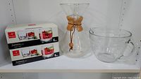 Two boxed sets of Bormioli Galassia glasses, vintage Pyrex Chemex coffee maker decanter with wood and leather, and glass measuring cup on a shelf.