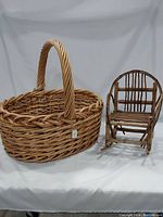 Photo showing extra large round woven wood basket with thick, twisted wood handle and assorted craft wood pieces inside, next to rustic bent twig rocker chair with curved back and rockers.