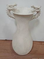Front full view of a large tall white textured plaster planter vase with dragon head handles on each side near the rim.