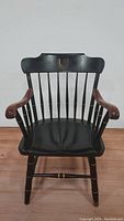 Front view of the black wooden captain's chair showing spindle back and curved arms with gold accents.