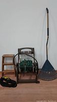 Group shot showing 2-step wooden ladder, metal hose reel with green vinyl garden hose, black flex garden hose coiled, and blue leaf rake with bent handle.