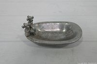 Top and angled side view of the vintage pewter soap dish shaped like a bath tub with faucet handles