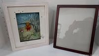 View showing framed Jean Pierre Weill vitreograph glass art of Pooh and Piglet next to a separate empty picture frame.