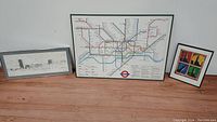 Three framed art pieces side by side: panoramic sketch on left, London subway map center, colorful pop art print right.