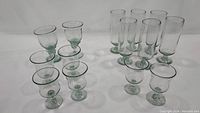 Group of short and tall green tinted handblown glasses on white background