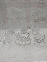 Six crystal and glass items shown together on a quilted pink and white background; including a petal-shaped bowl, a small square dish, and other assorted bowls and dishes