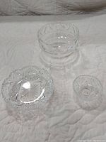 Front angle photo showing all three crystal bowls on a white quilted surface; the larger Tiffany lead crystal bowl with raised heart rim positioned behind two smaller Brilliant Period cut glass bowls.